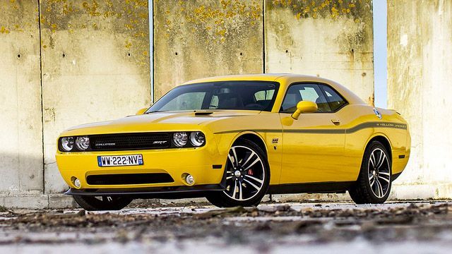 Yellow muscle car parked against a weathered concrete wall.