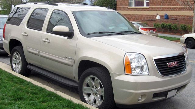 Beige GMC SUV parked on a residential street beside a brick building