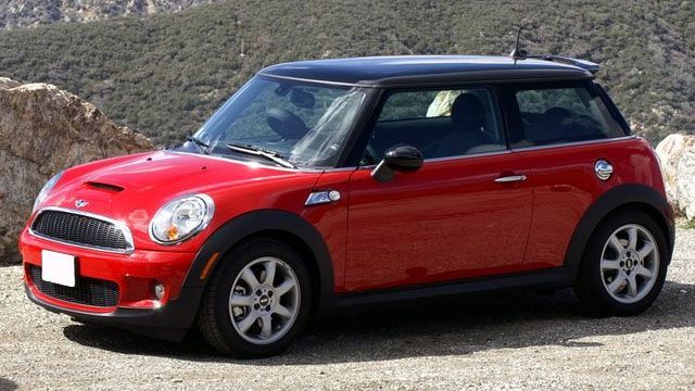 Red Mini Cooper parked on a rocky roadside by the water under a sunny sky.