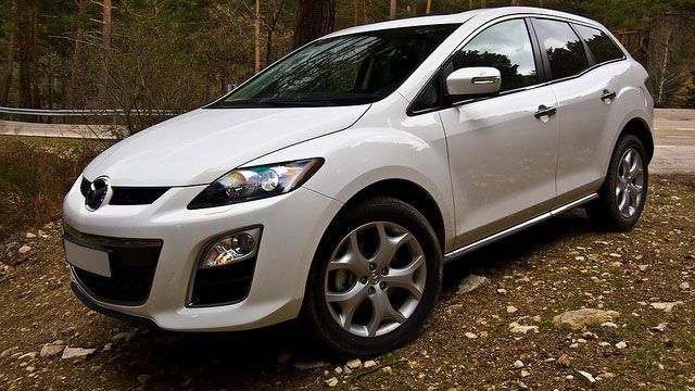 White SUV parked on a wooded dirt road, angled front view.