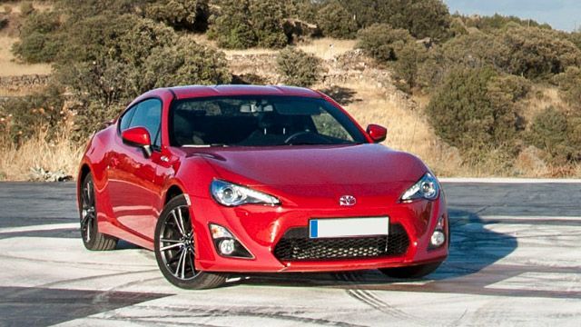 Red sports coupe parked on a road with dry hills in the background