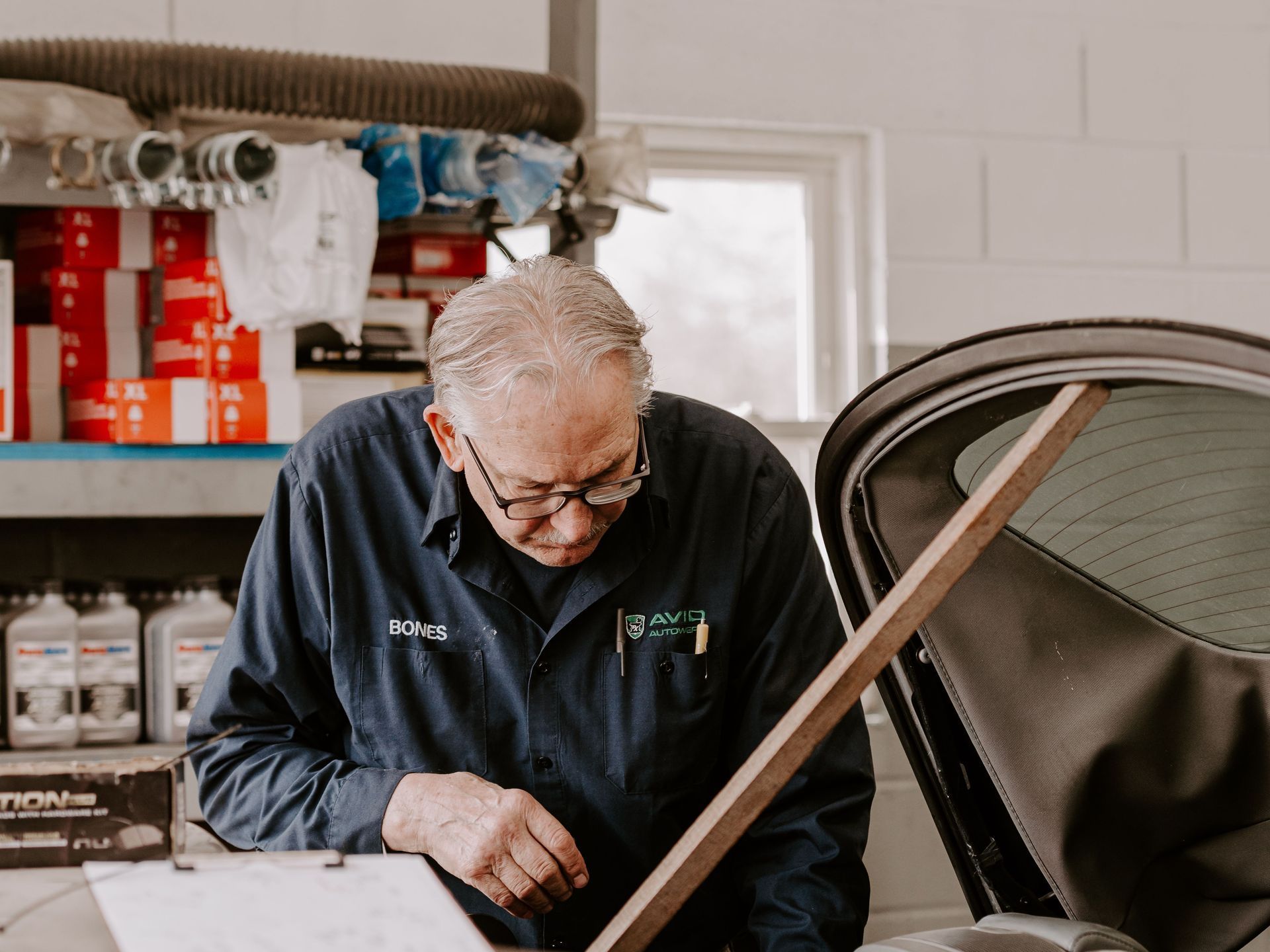 Mechanic inspecting a car in a garage, leaning over the open hood.
