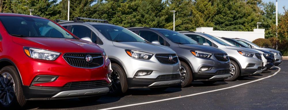 Row of parked sedans, including red, silver, and gray cars, lined up along a roadside
