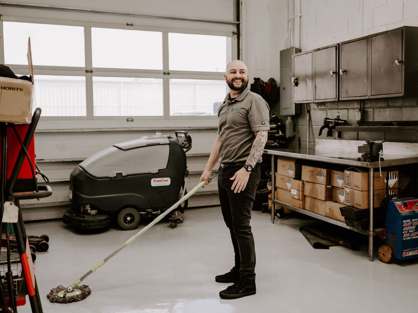 Man holding a floor scrubber in a workshop with tools and cabinets along the wall
