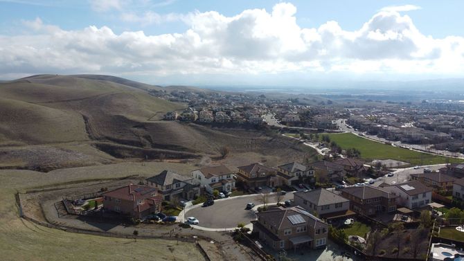 Panoramic view of a town beside green hills under a partly cloudy sky