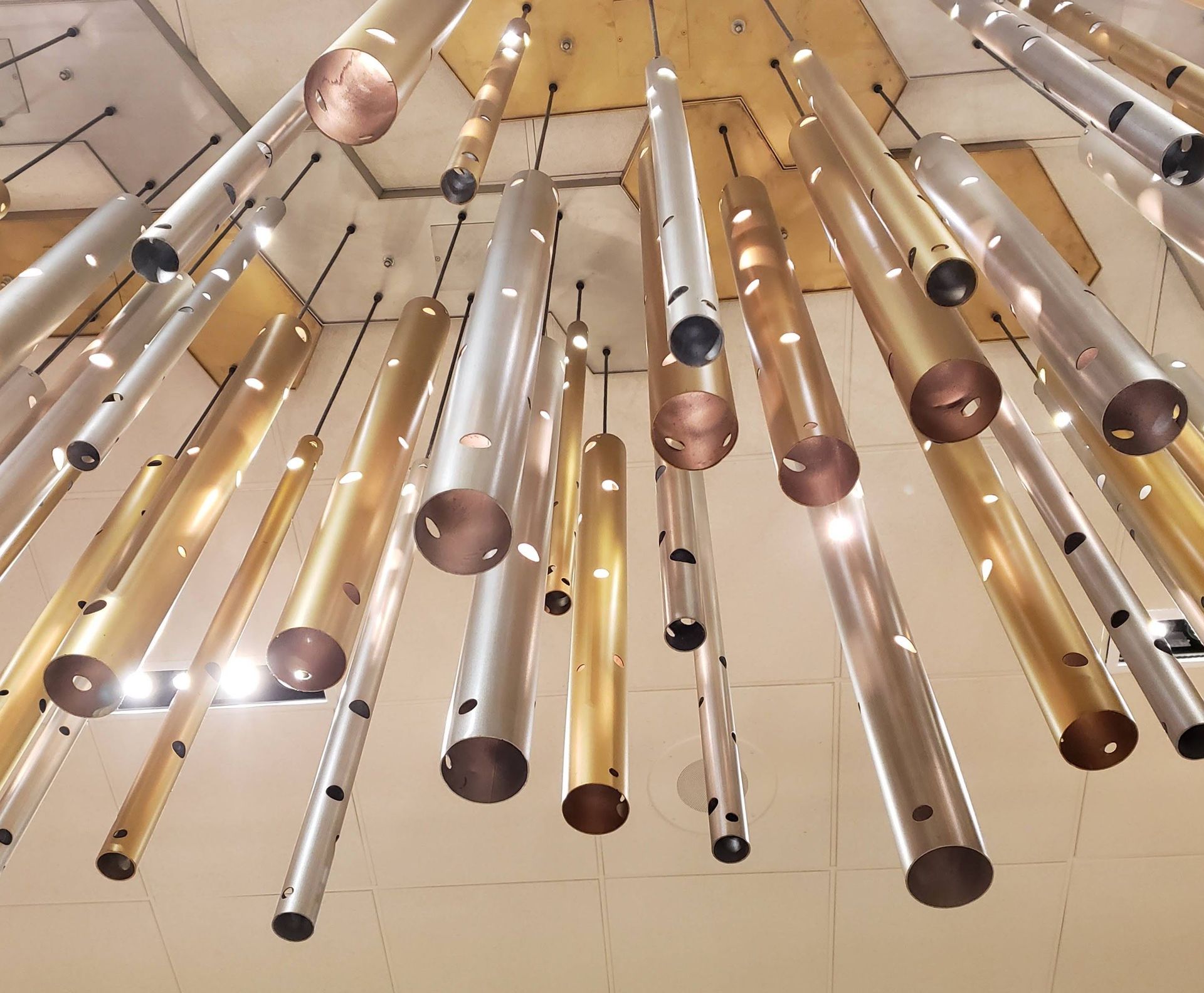 Hanging glass tubes and metallic rods suspended from a ceiling, viewed from below, in warm light