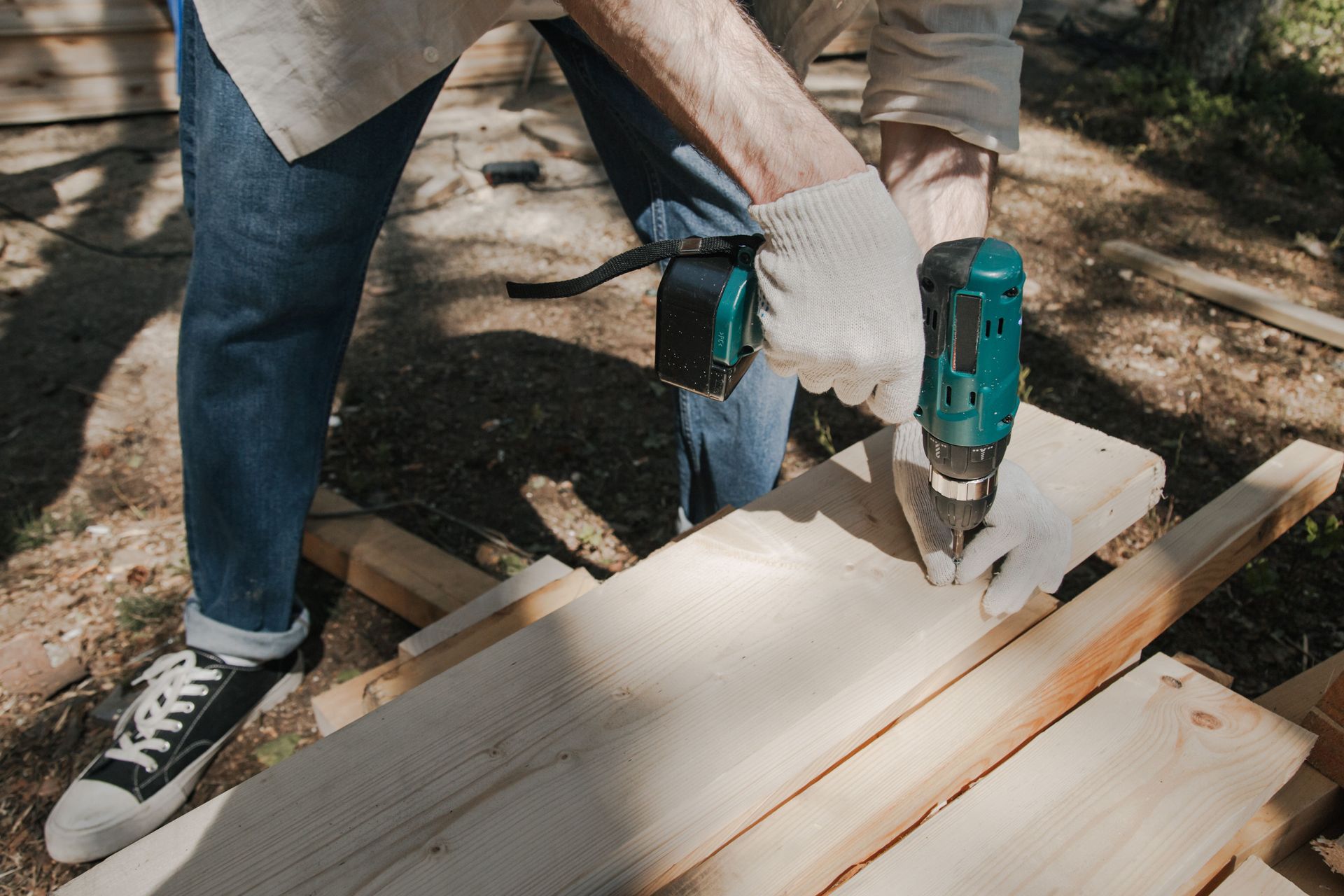 Person using a teal drill to fasten white boards outdoors on a workbench