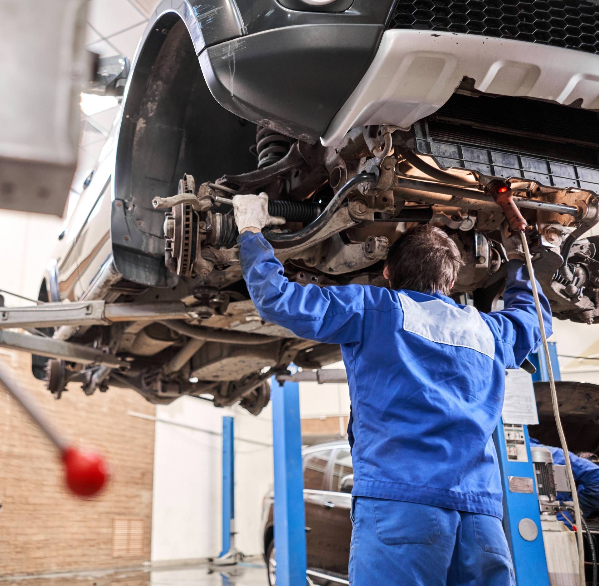 Mechanic in blue coveralls inspecting a car lifted on a repair hoist in an auto shop