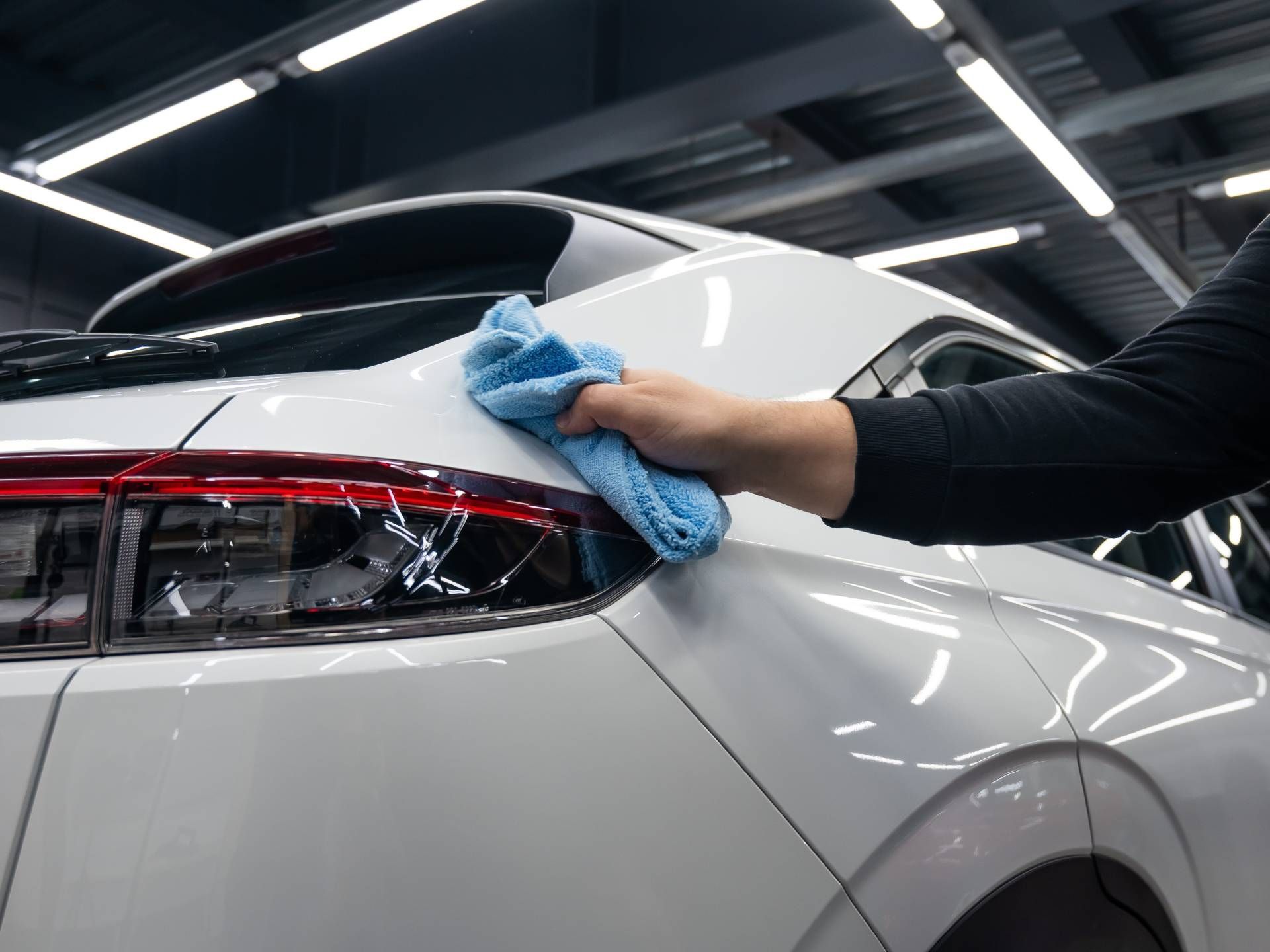 Hand wiping the rear of a white car with a blue cloth in a garage
