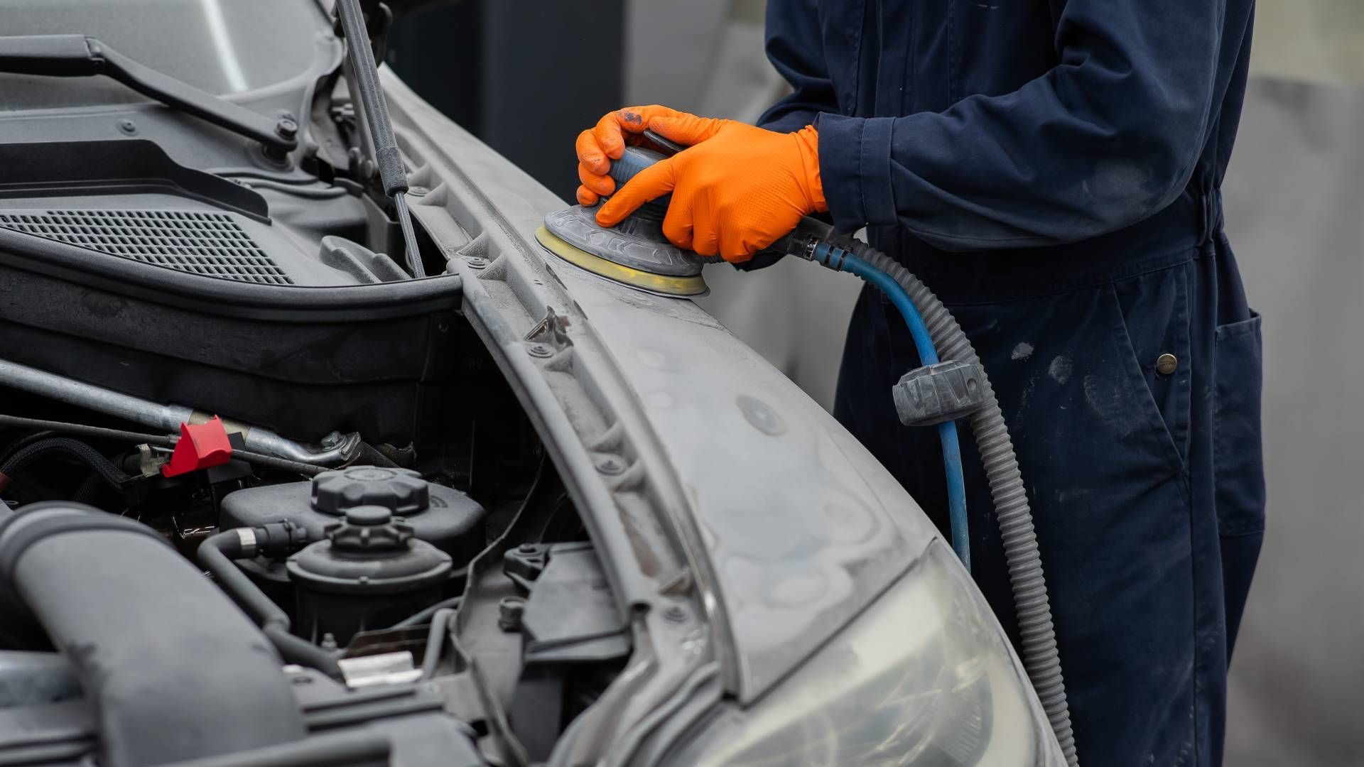 Mechanic in orange gloves inspecting a car engine with the hood open