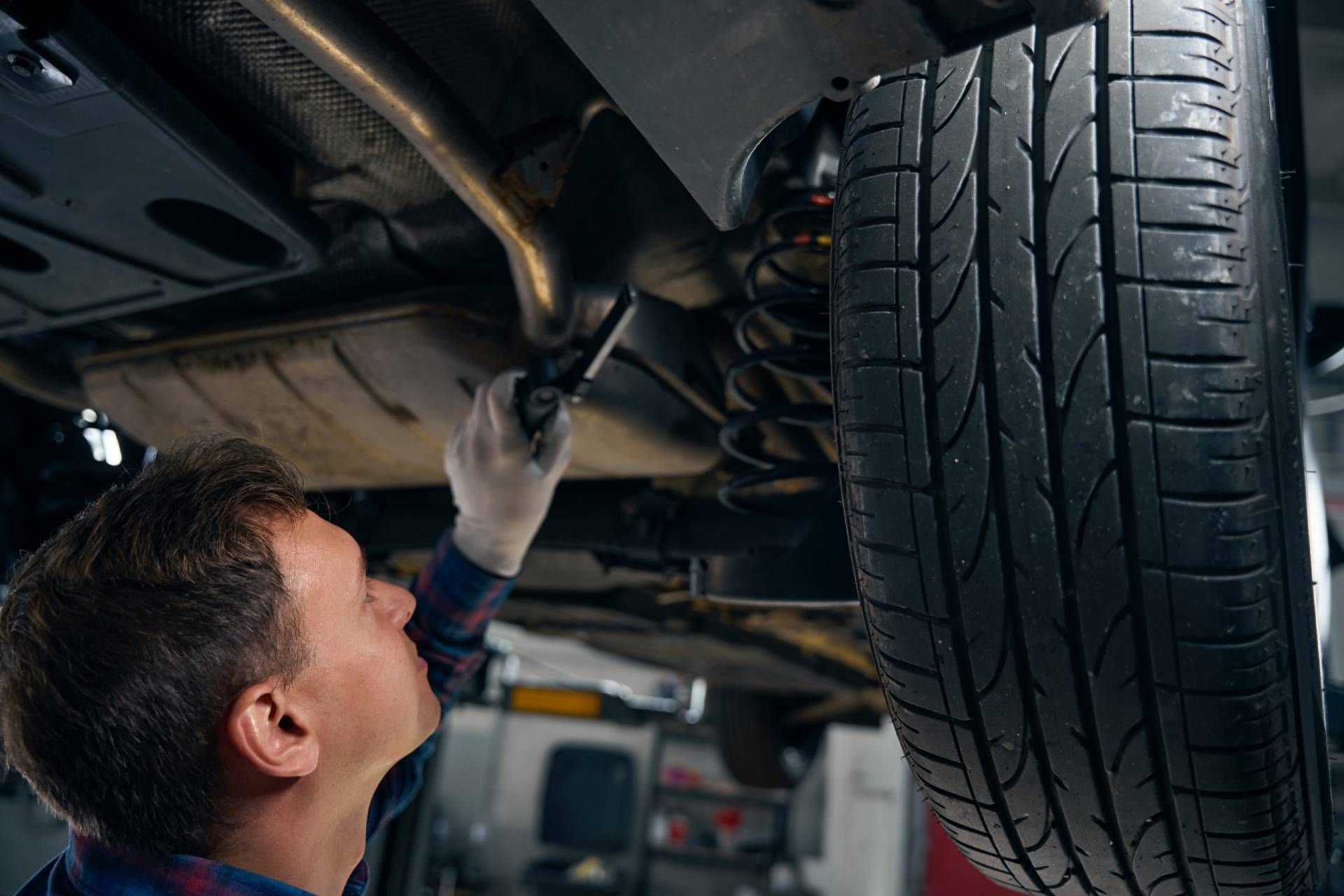 Mechanic inspecting a car’s undercarriage beside a raised tire in a garage
