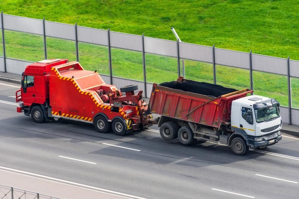 A Red Tow Truck is Towing a Dump Truck on a Highway — Bulahdelah Towing In Coolongolook, NSW