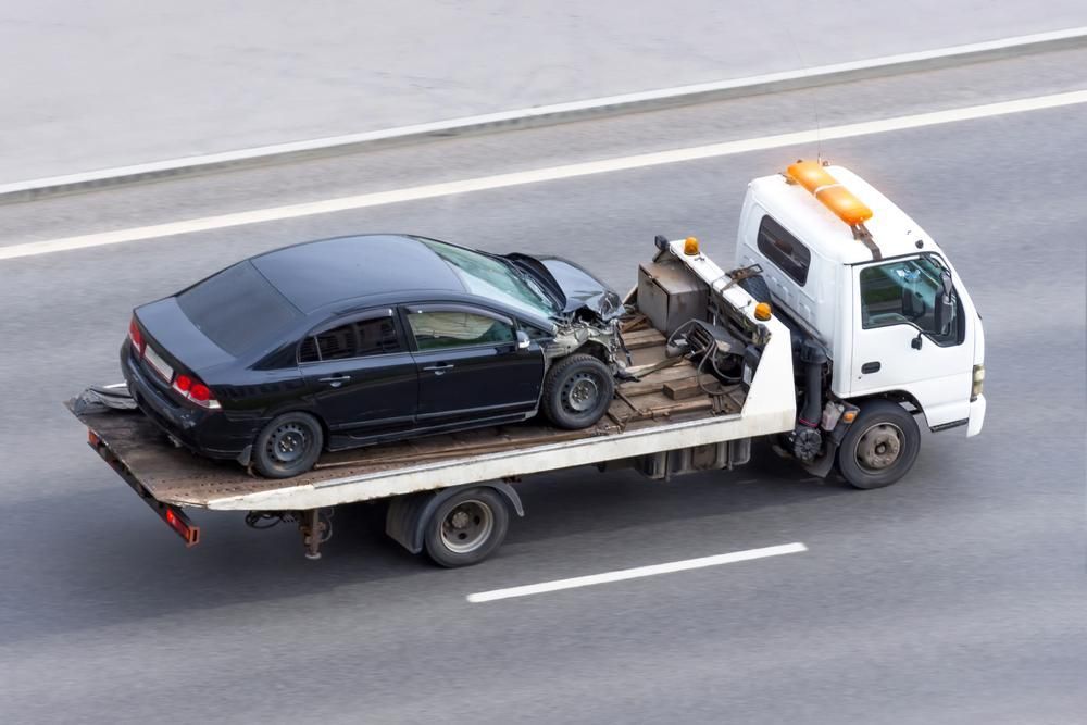 A Tow Truck is Towing a Black Car on a Highway — Bulahdelah Towing In Bulahdelah, NSW