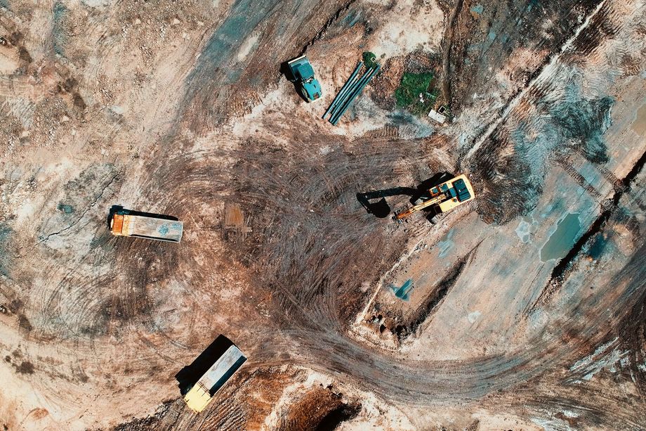 Aerial view of an excavation site with a few vehicles and dirt tracks on bare ground.