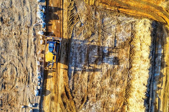 Yellow farm machinery harvesting a field of cut grain with a tree line in the background