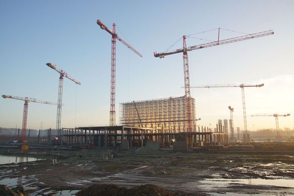 Construction site with multiple cranes and a partially built structure at sunset