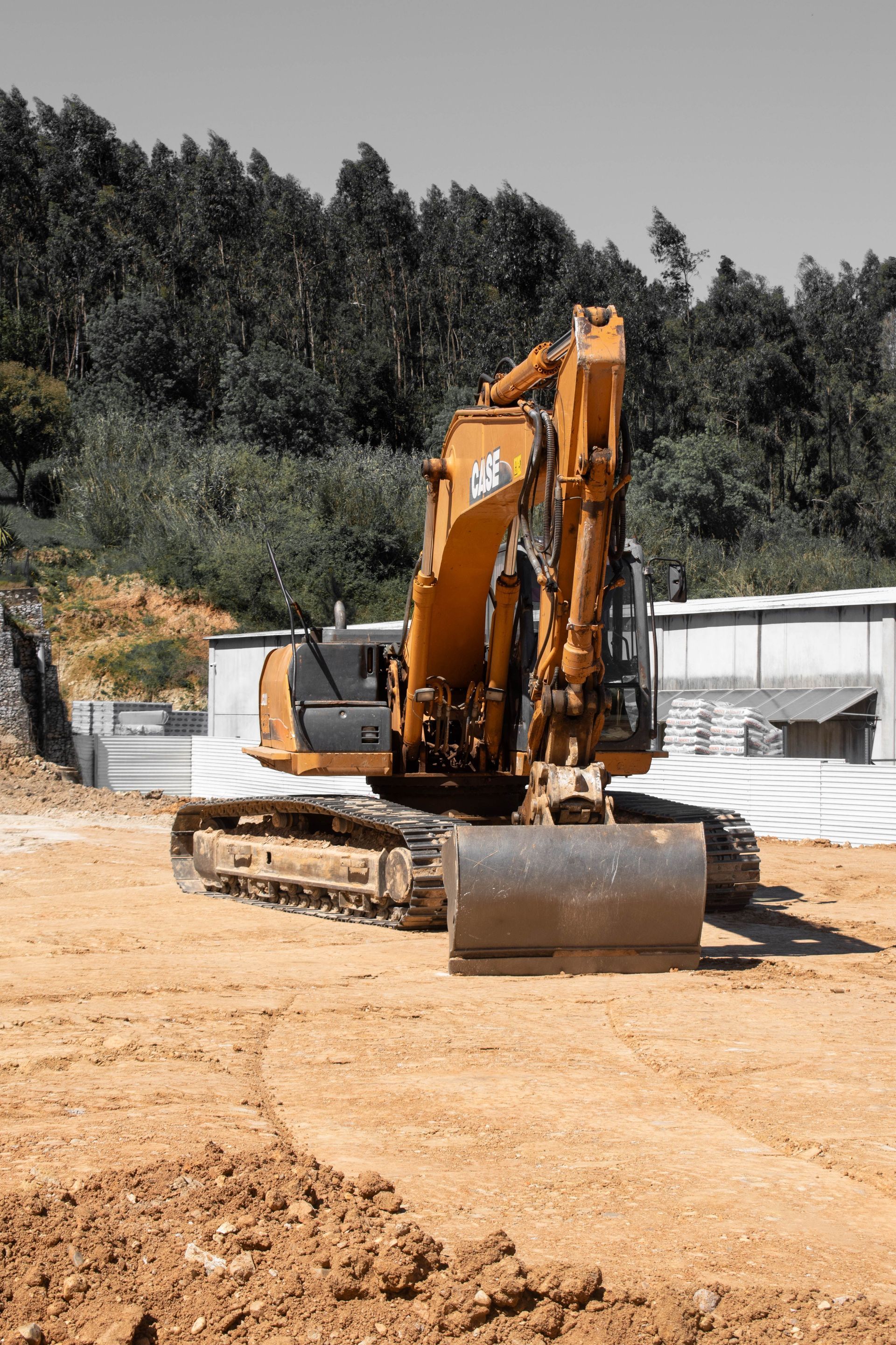 Orange excavator on dirt site with trees and stacked materials in the background
