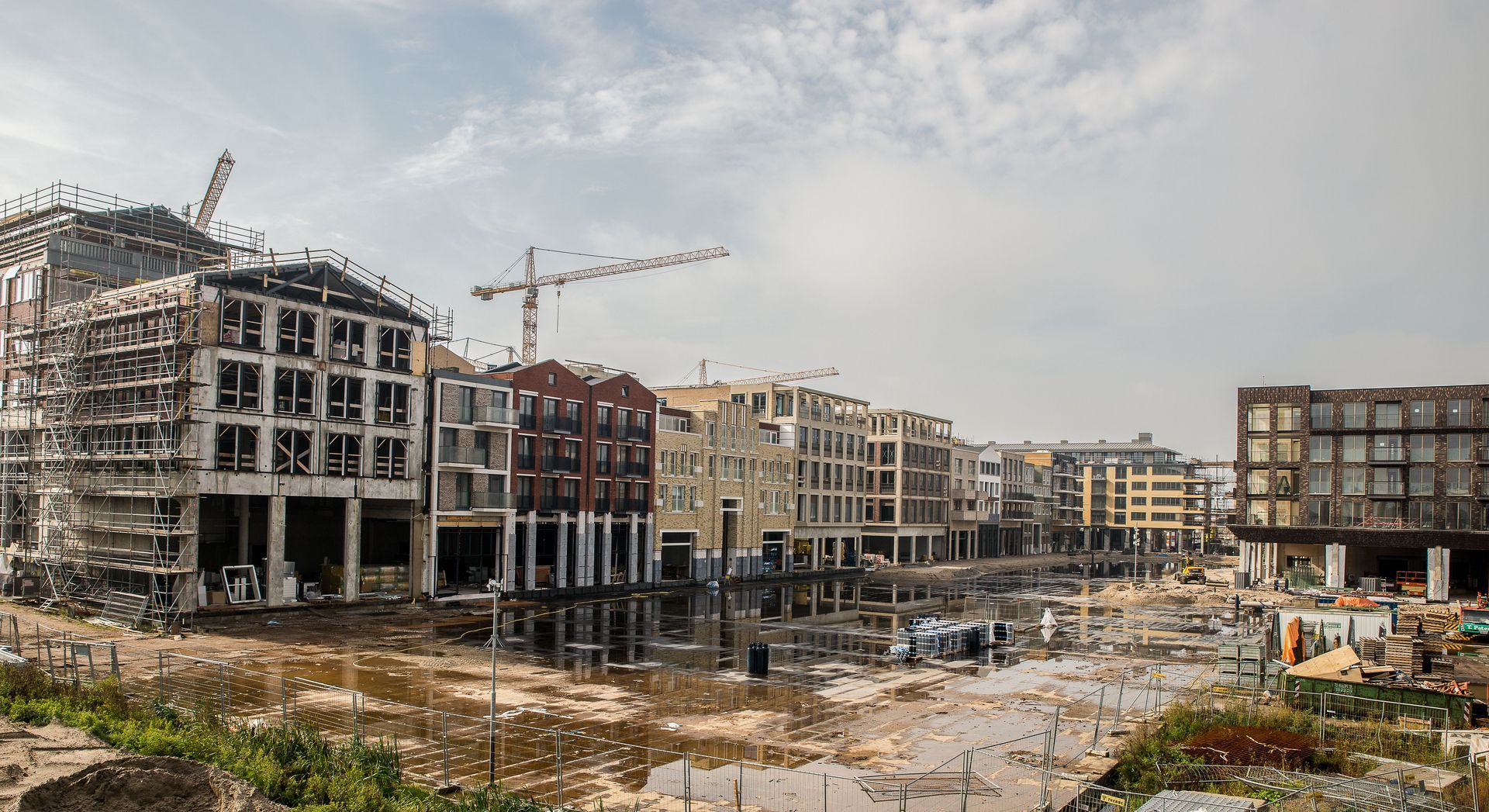 Construction site with unfinished apartment buildings, cranes, and piles of debris under a cloudy sky