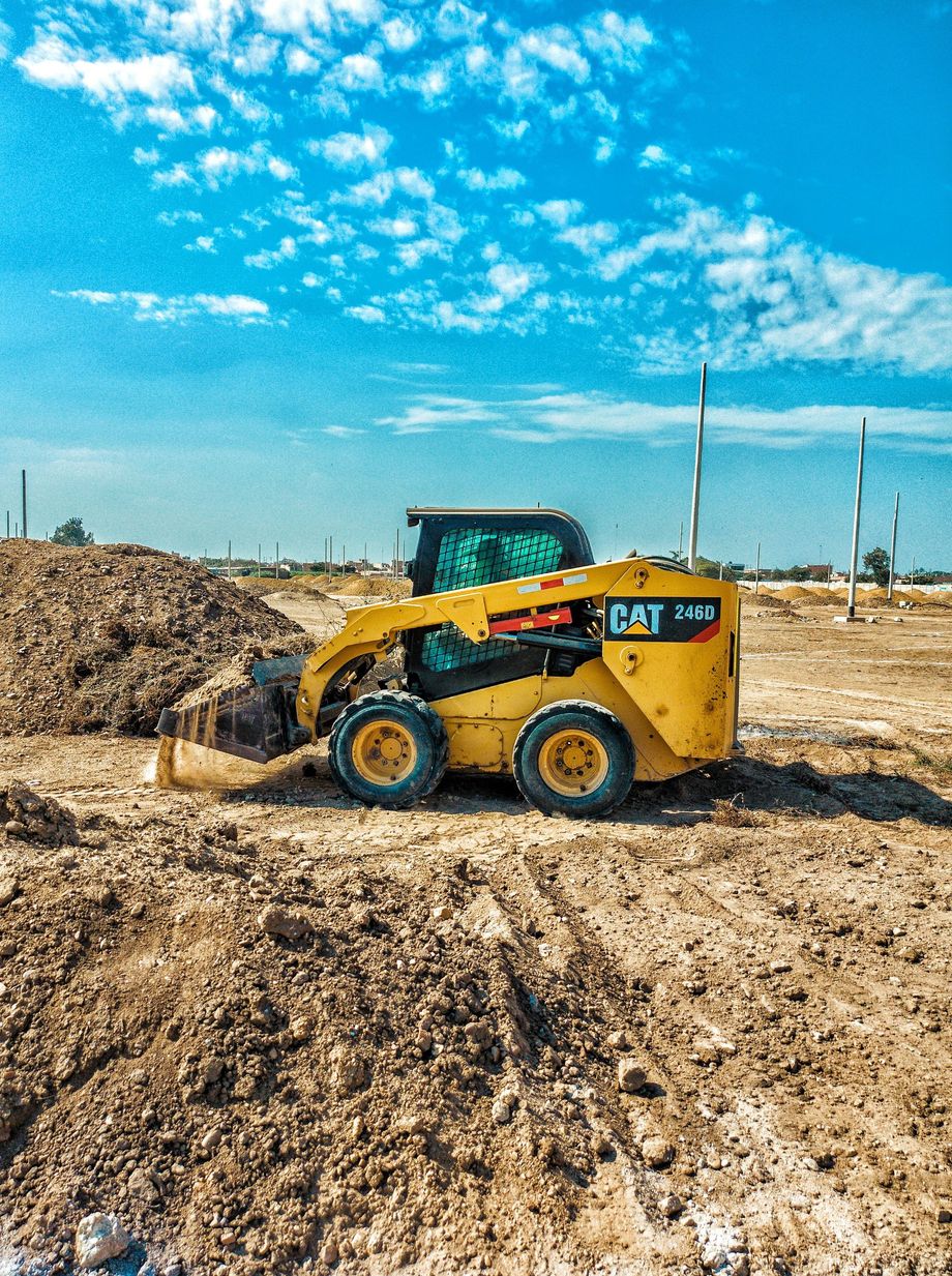 Yellow skid steer loader working in a dirt lot under a bright blue sky