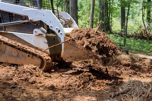 White bulldozer pushing dirt in a wooded clearing