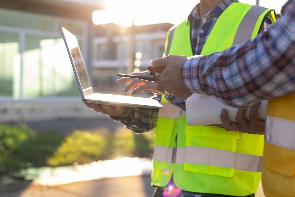 Construction worker in neon safety vest using a laptop at a building site