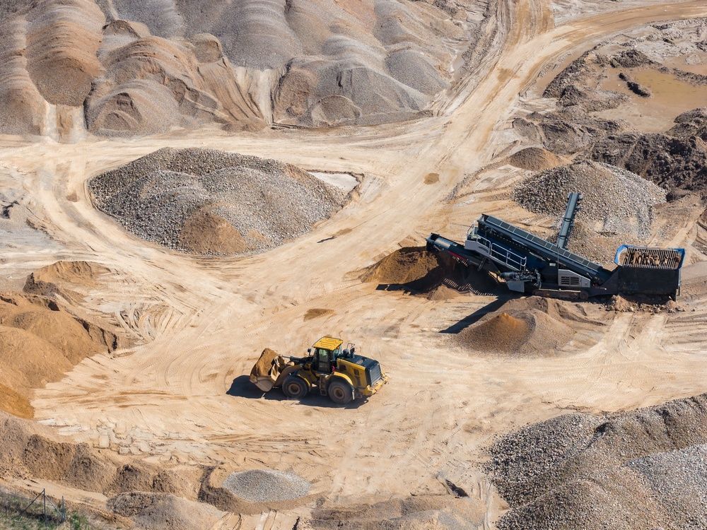 Bulldozer and conveyor machines working in a dusty open-pit quarry.