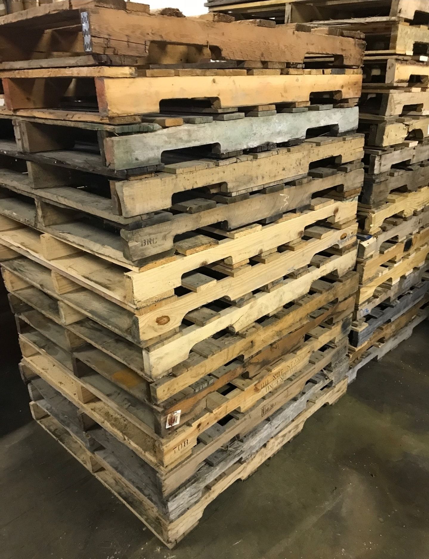 Stacks of worn wooden pallets piled in a warehouse aisle.