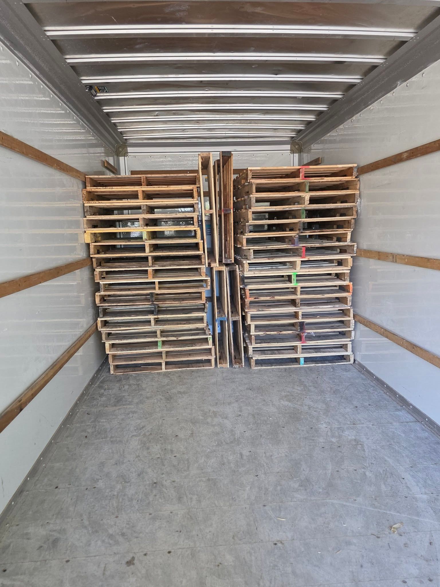 Empty moving truck interior with stacked wooden pallets at the front and a gray floor.