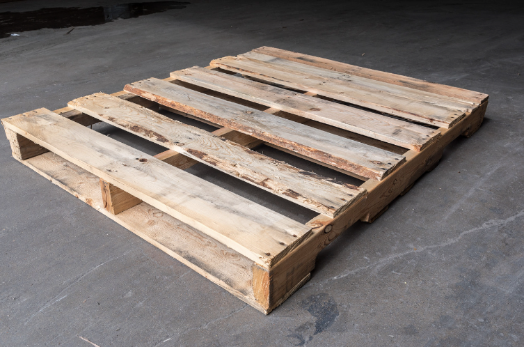 Wooden shipping pallet on a dark concrete floor.