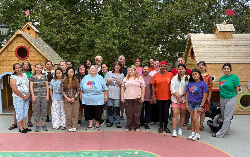 Group of people standing outdoors, posed near wooden playhouses, on a red and green surface.