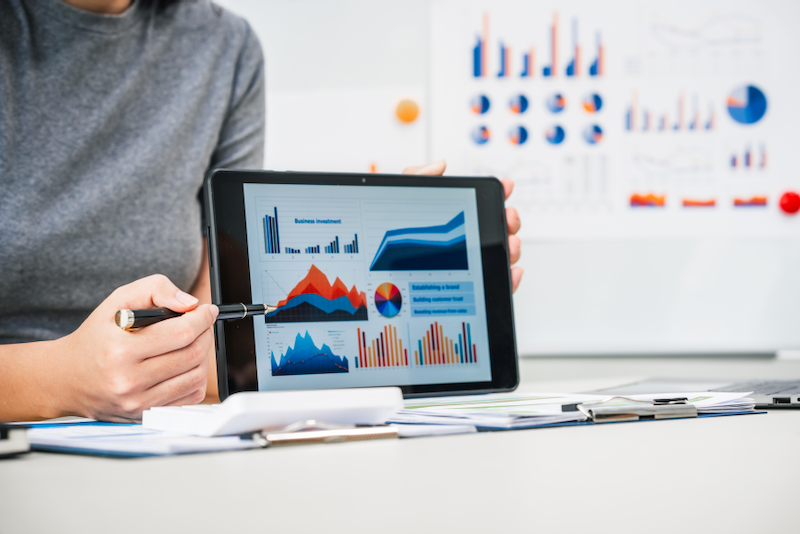 A woman is holding a tablet with graphs on it.