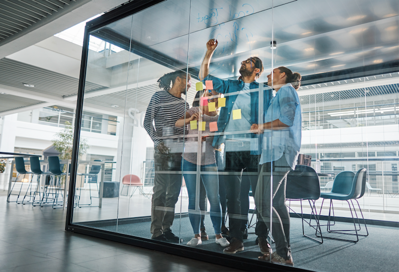 A group of people are standing around a glass wall with sticky notes on it.