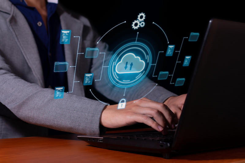 A person is typing on a laptop computer with a cloud icon on the screen.
