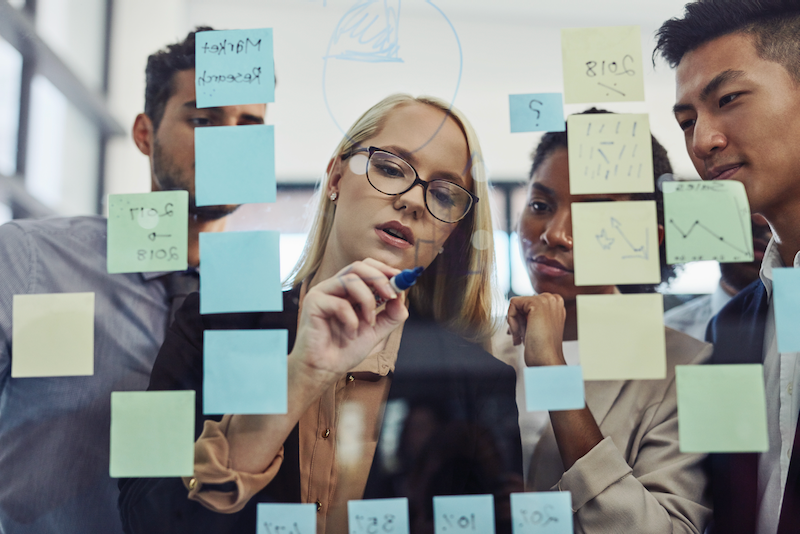 A group of people are looking at sticky notes on a glass wall.