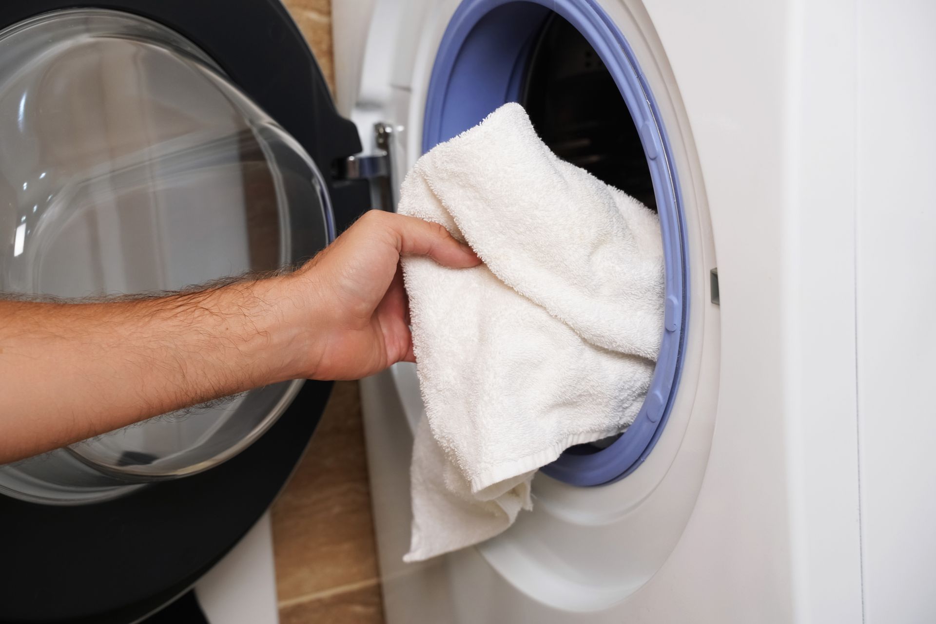 Hand placing a white towel into a front-loading washing machine