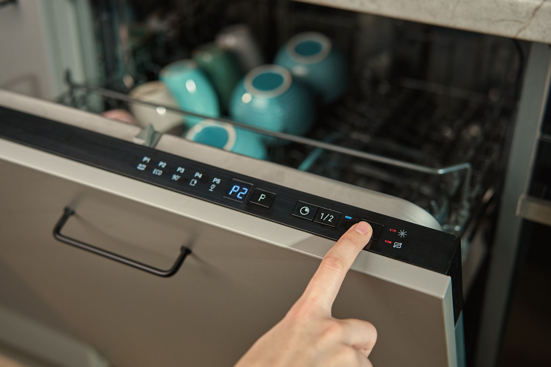 Hand pressing a touch-control panel on a dishwasher with blue-lit display and dishes inside