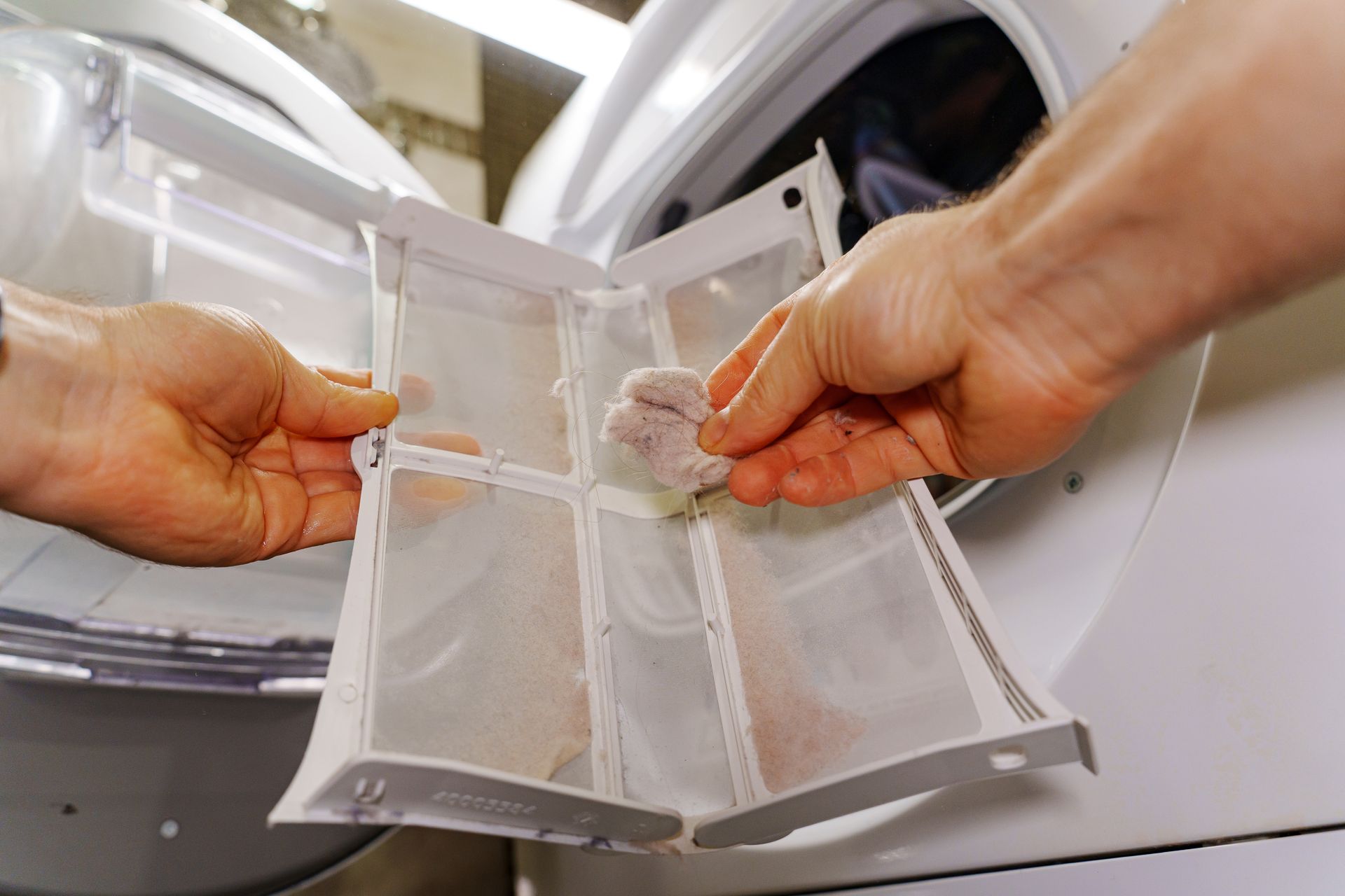 Hands removing a lint filter from a front-loading washing machine