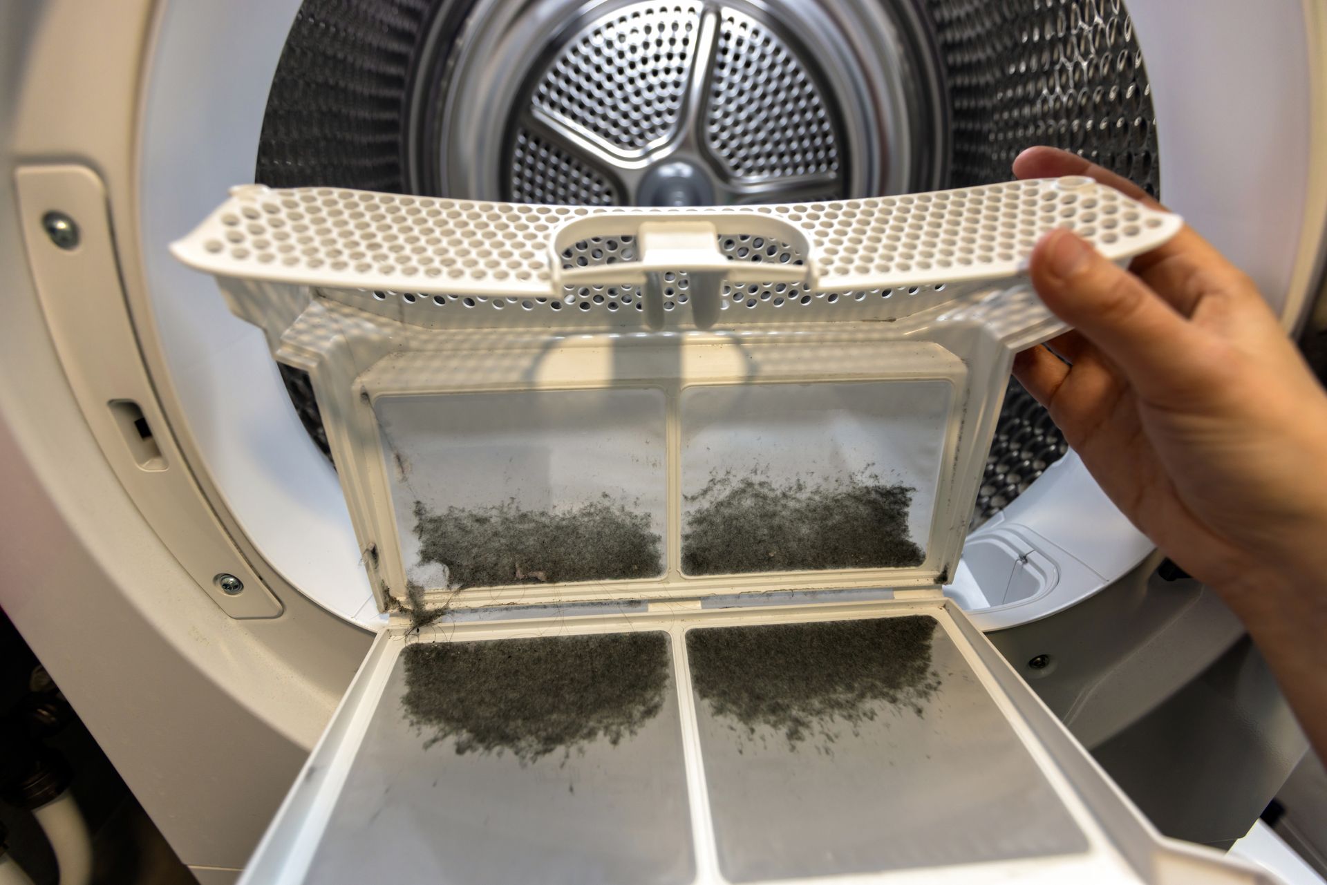 Hand holding a lint filter covered with gray dryer lint in a washing machine drum