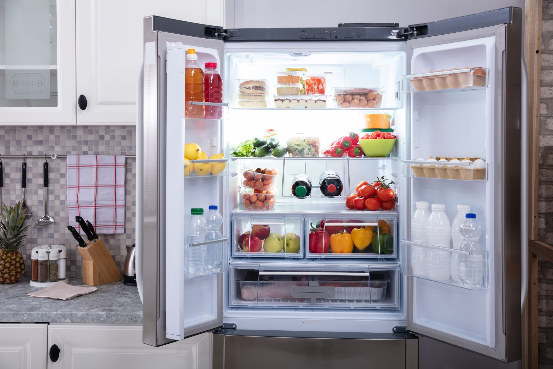 Open refrigerator stocked with fruits, vegetables, drinks, and condiments in a kitchen