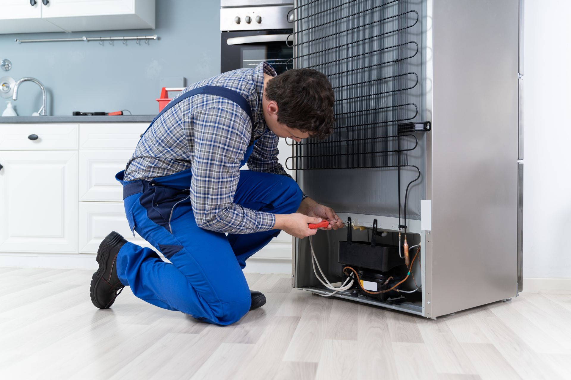 Technician repairing a refrigerator in a modern kitchen with tools and the lower panel open