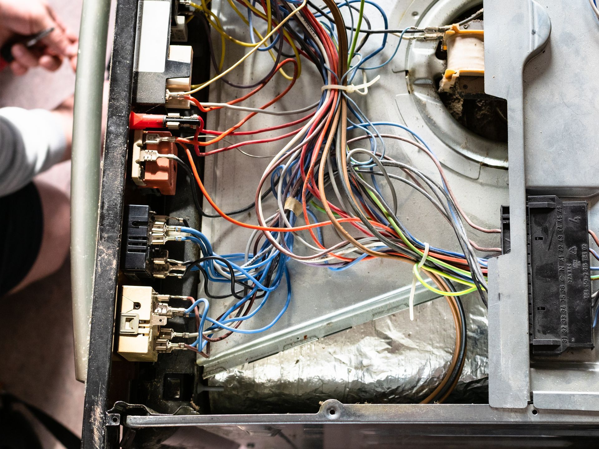 Open electrical control panel with tangled multicolored wires and circuit breakers exposed