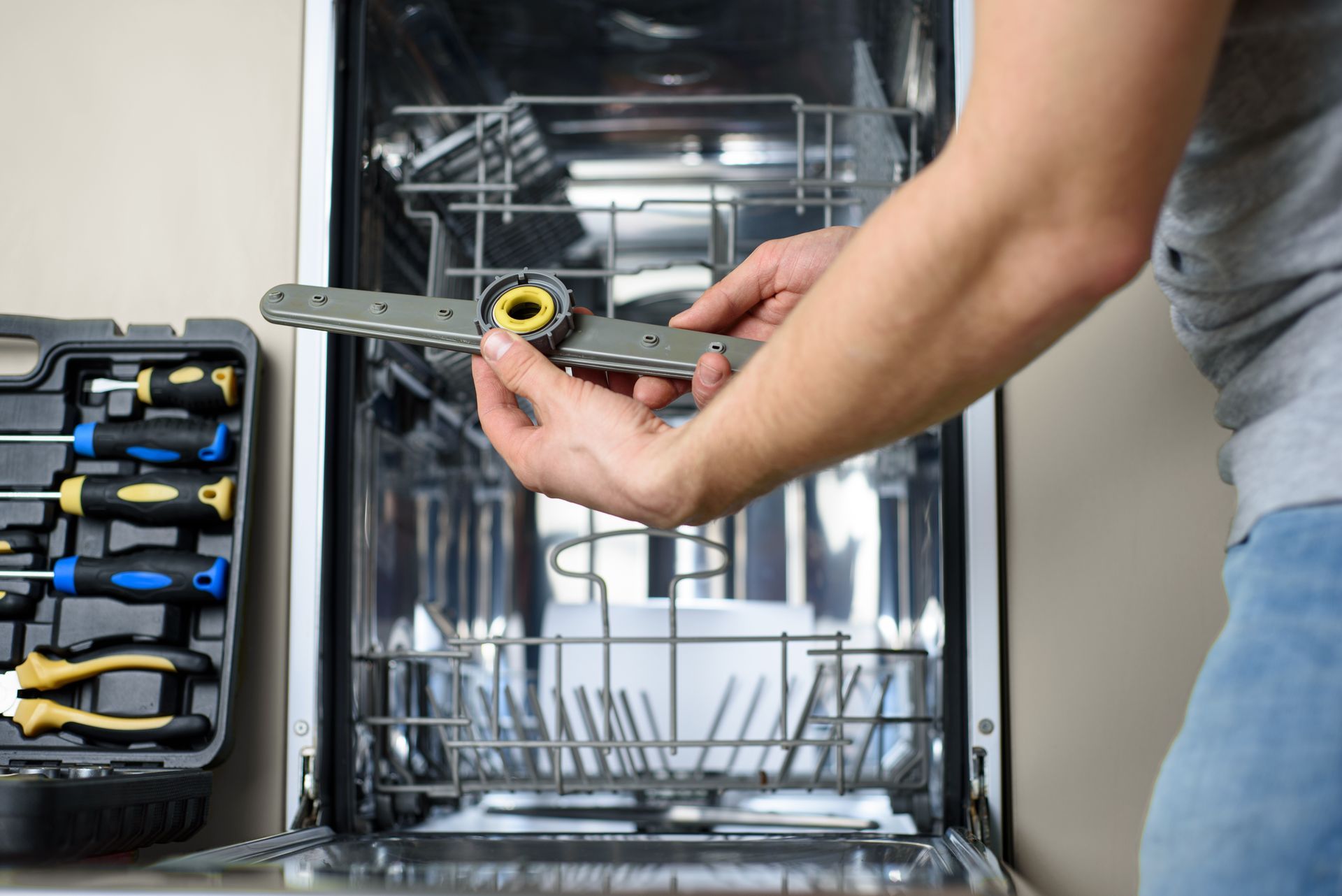 Person holding a wrench near an open dishwasher with tools on the left side shelf