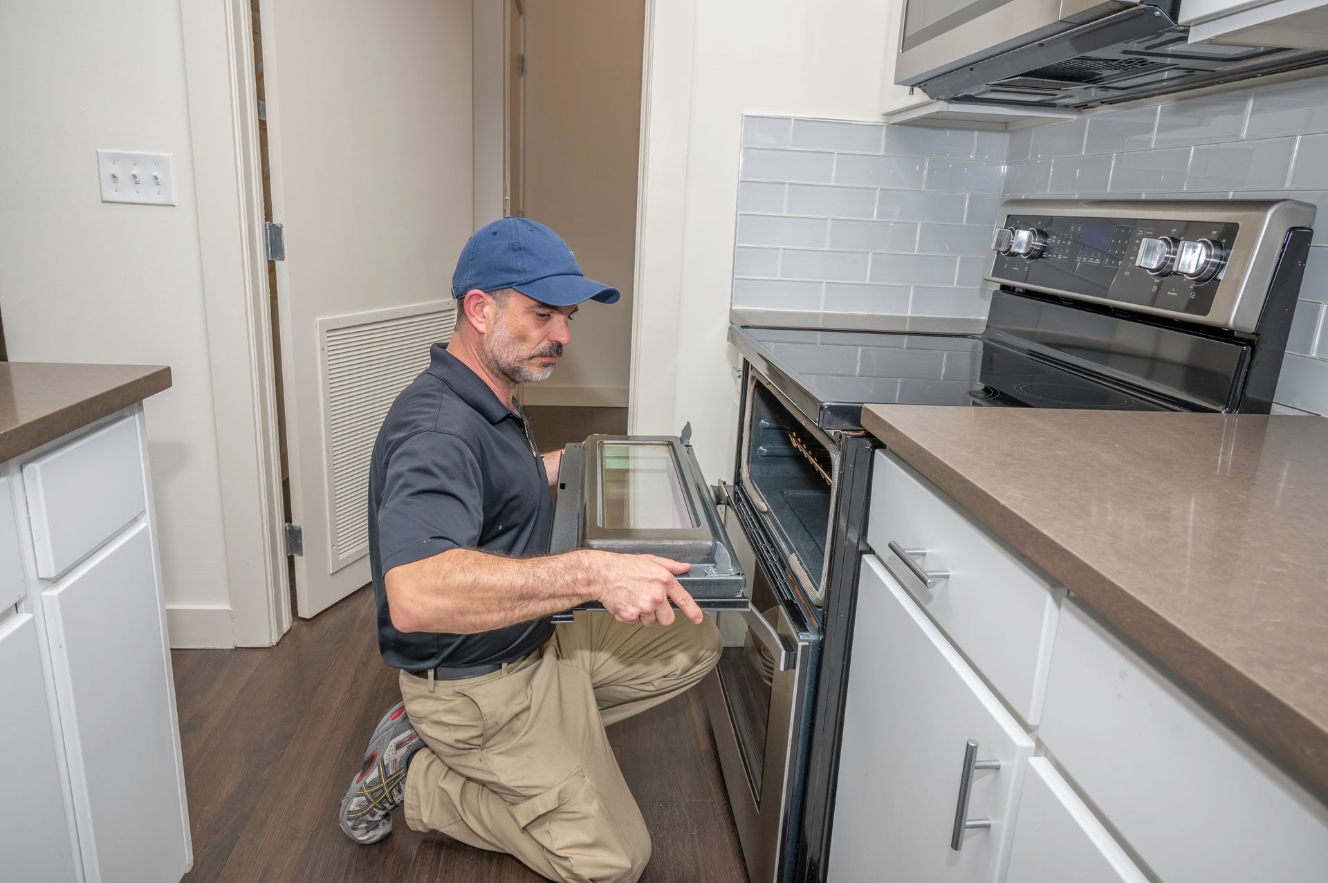 Person kneeling in a kitchen, cleaning a black oven with a sponge.