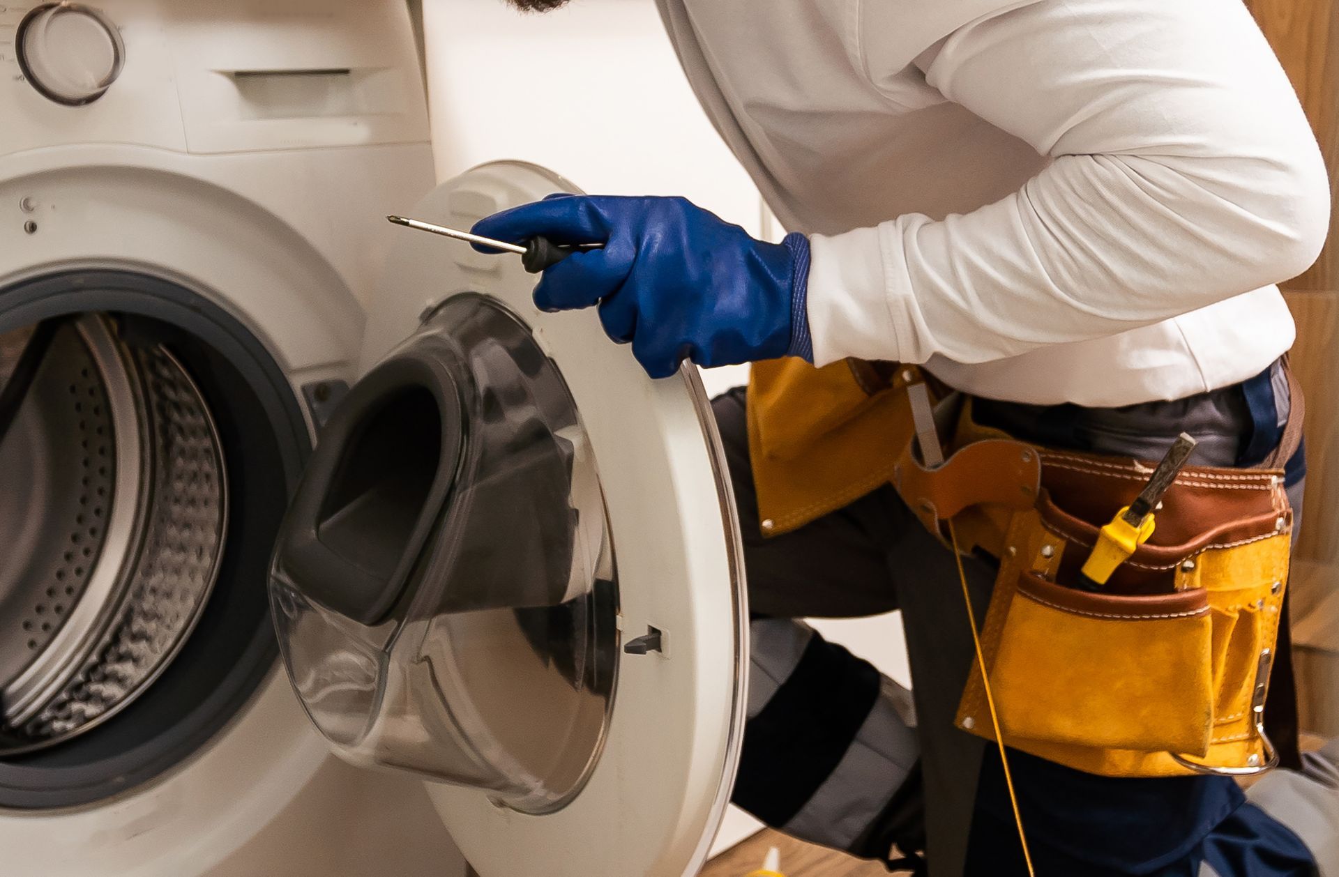 Technician in blue gloves working on an open front-loading machine with a yellow tool belt