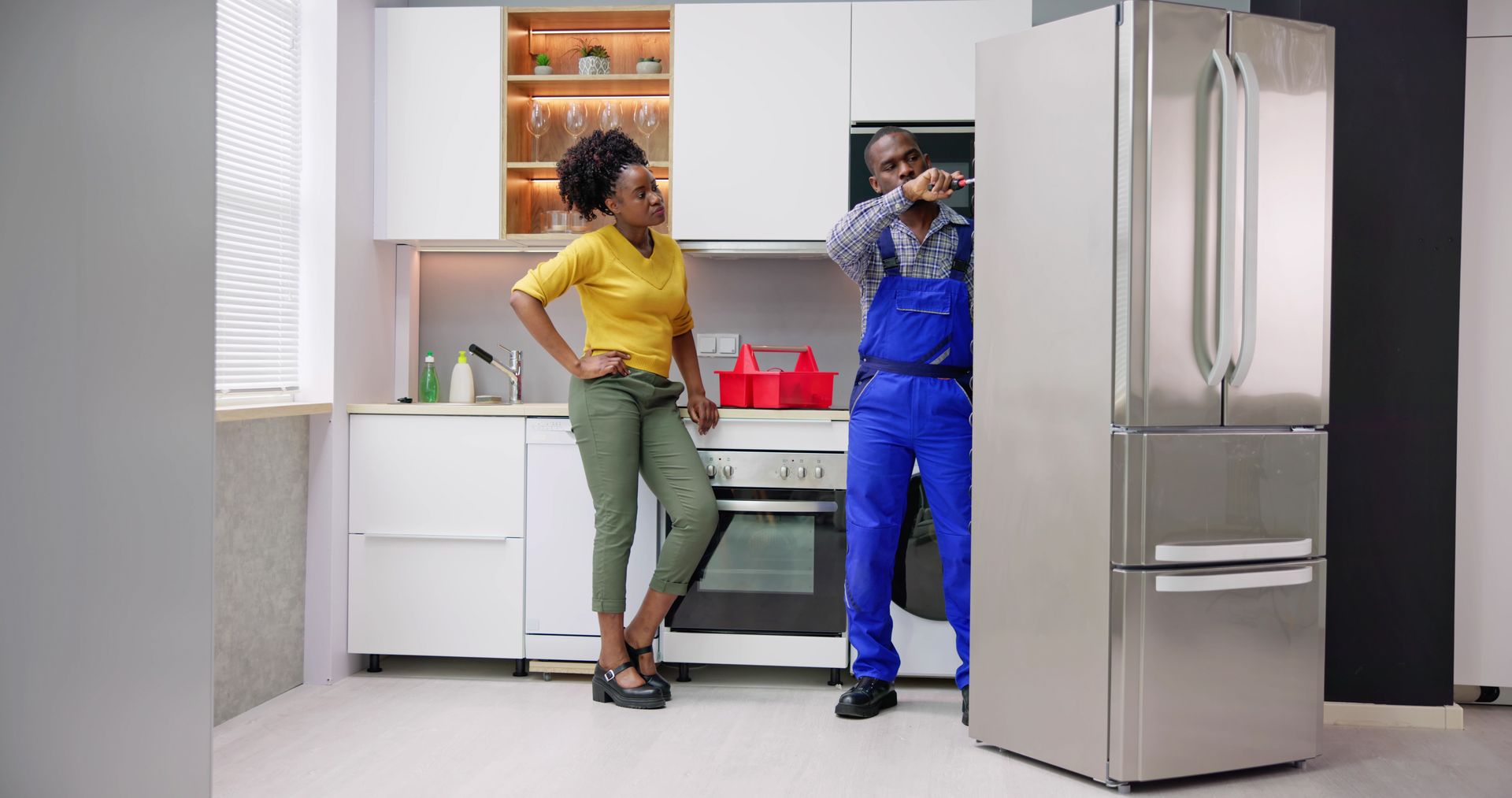 Two people talking in a modern kitchen beside a stainless steel refrigerator.