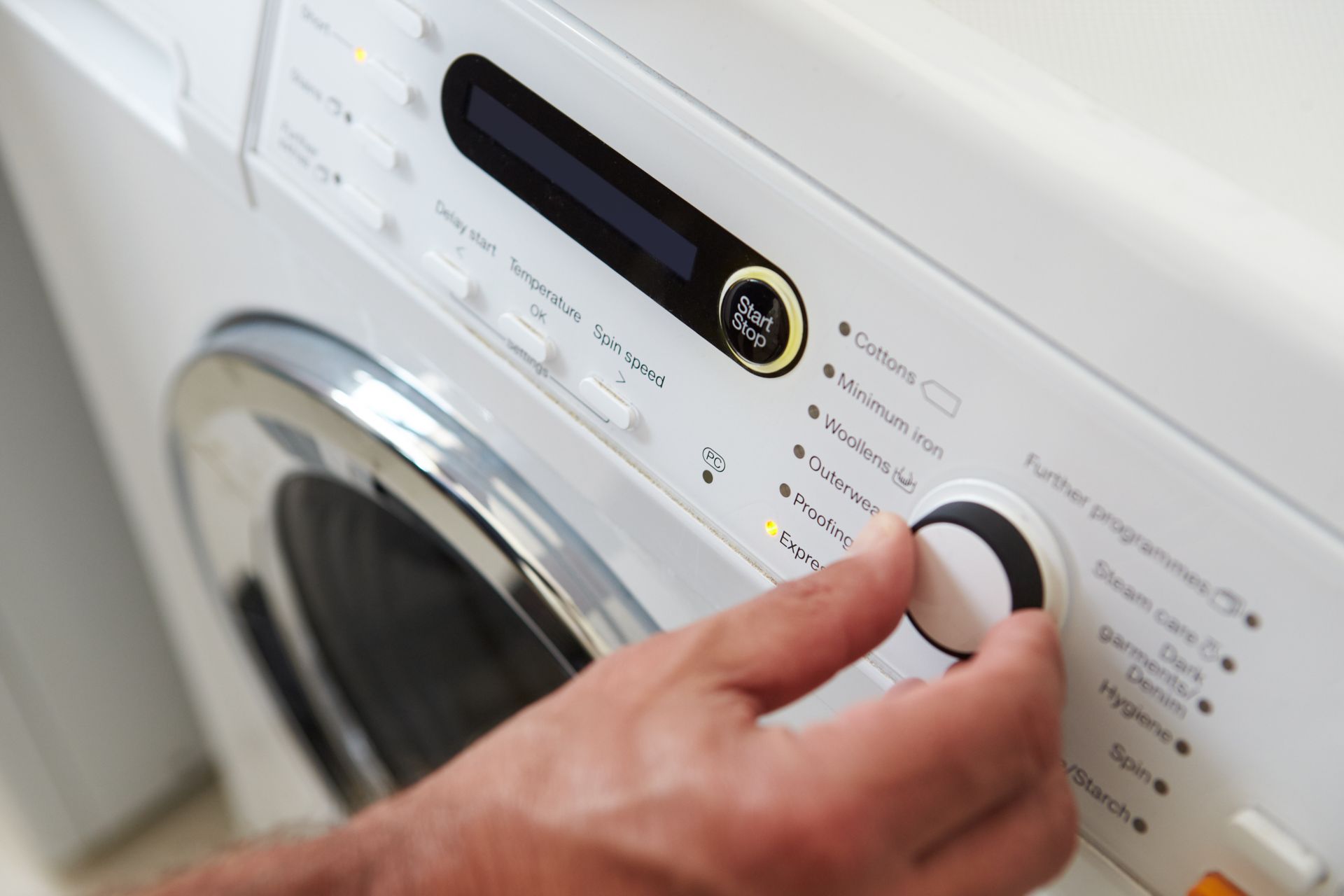 Hand adjusting a washing machine control dial on a white front-loading washer