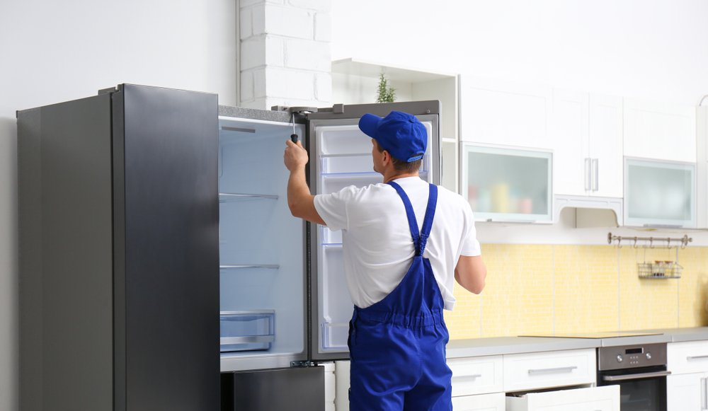 Person in blue overalls opening a refrigerator in a bright kitchen