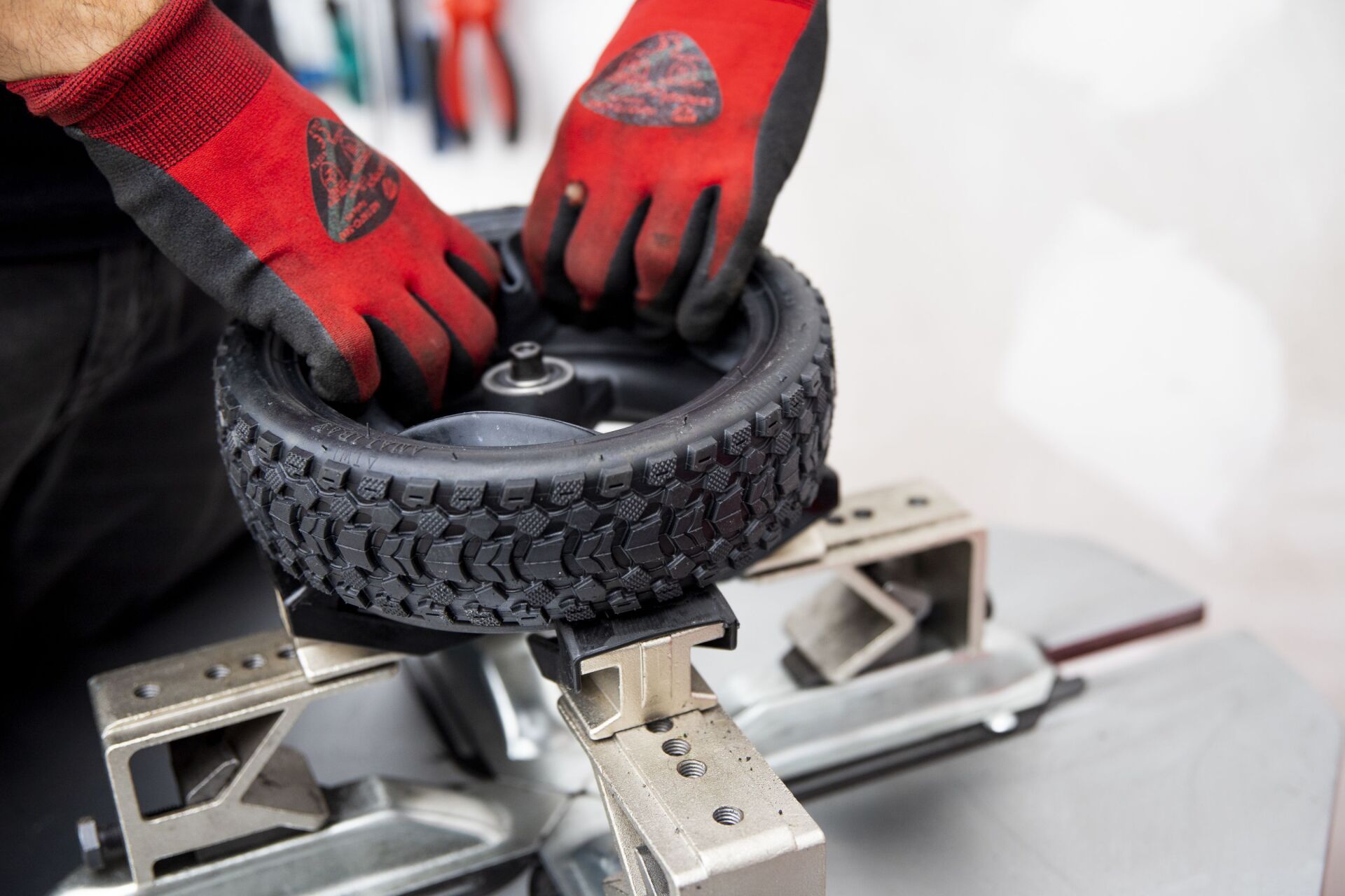 Unas manos con guantes rojos sujetan un neumático pequeño a un soporte metálico para su mantenimiento.