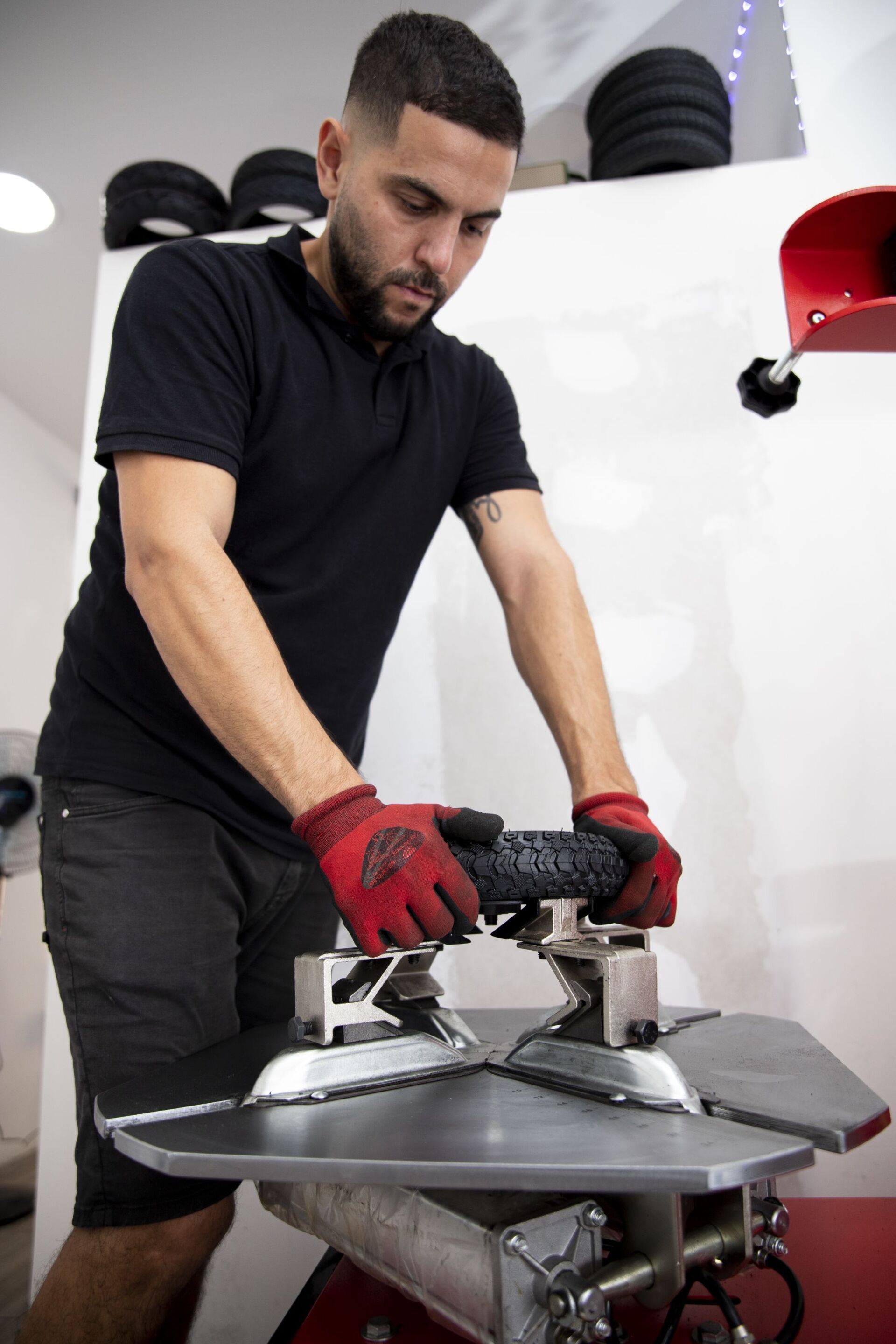En un taller, una persona que lleva guantes de trabajo rojos utiliza una máquina para sujetar un neumático pequeño y texturizado.