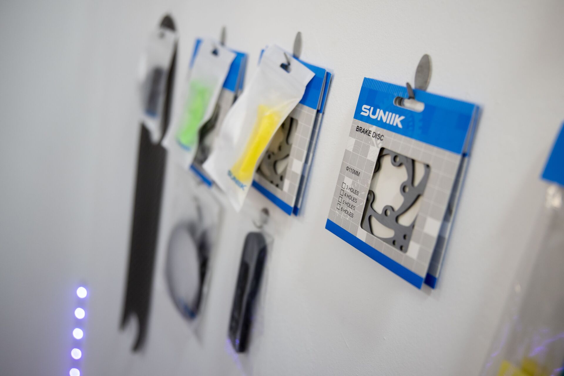 En un expositor de pared blanca, con etiquetas de marca y herrajes metálicos, cuelgan piezas de bicicleta y herramientas empaquetadas.
